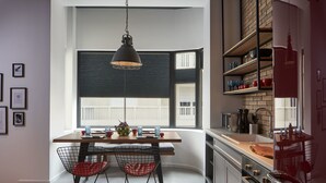 A modern kitchen with a dining area, featuring a wooden table, wire chairs, and a hanging light fixture.