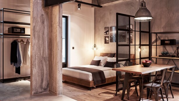 A bedroom with a wooden bed, a desk with chairs, a wardrobe, and a large window.