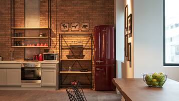 Una cocina con pared de ladrillo, un refrigerador rojo y una mesa con un cuenco de manzanas.