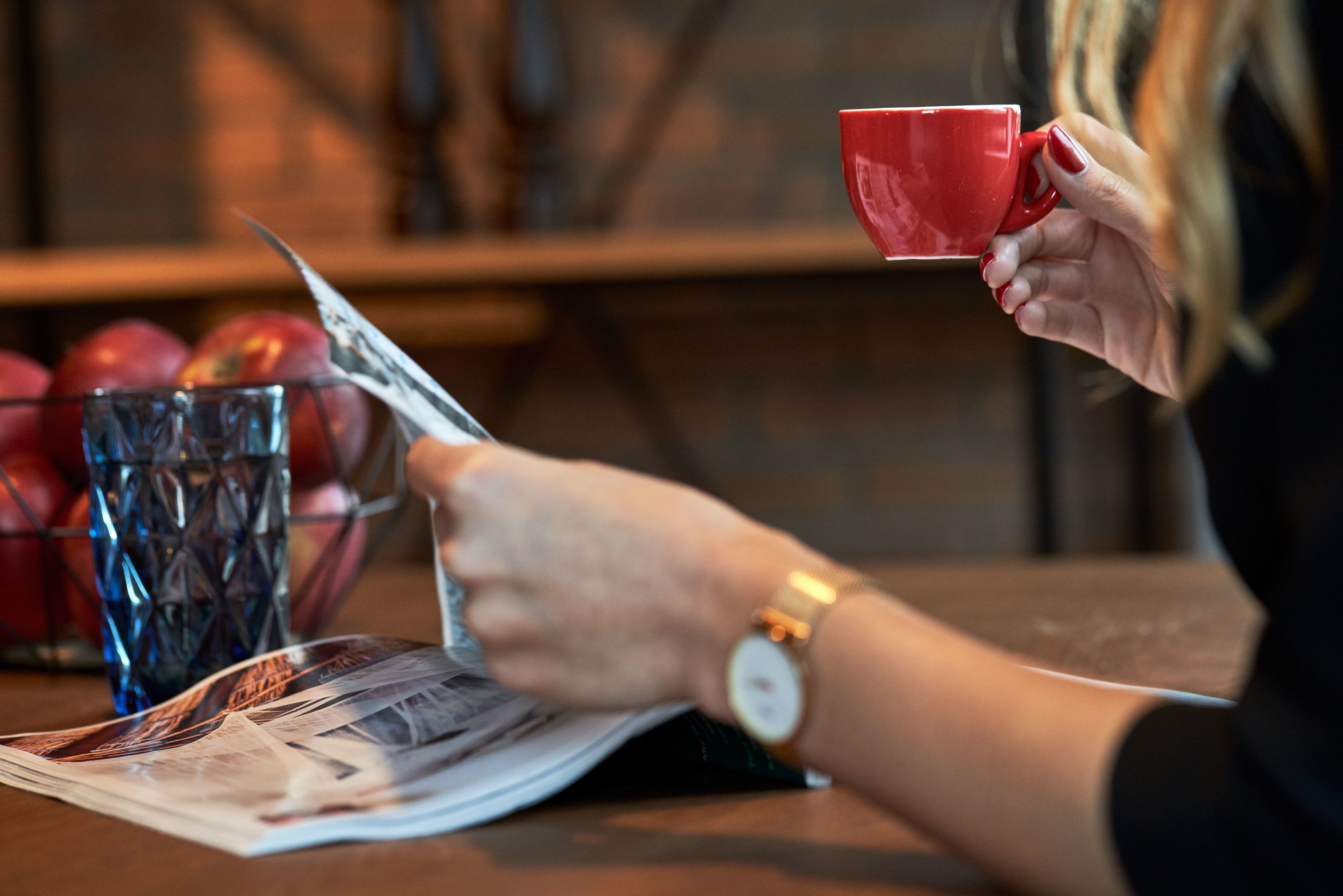 Iemand leest een krant met een rode beker en een glas water op een tafel.