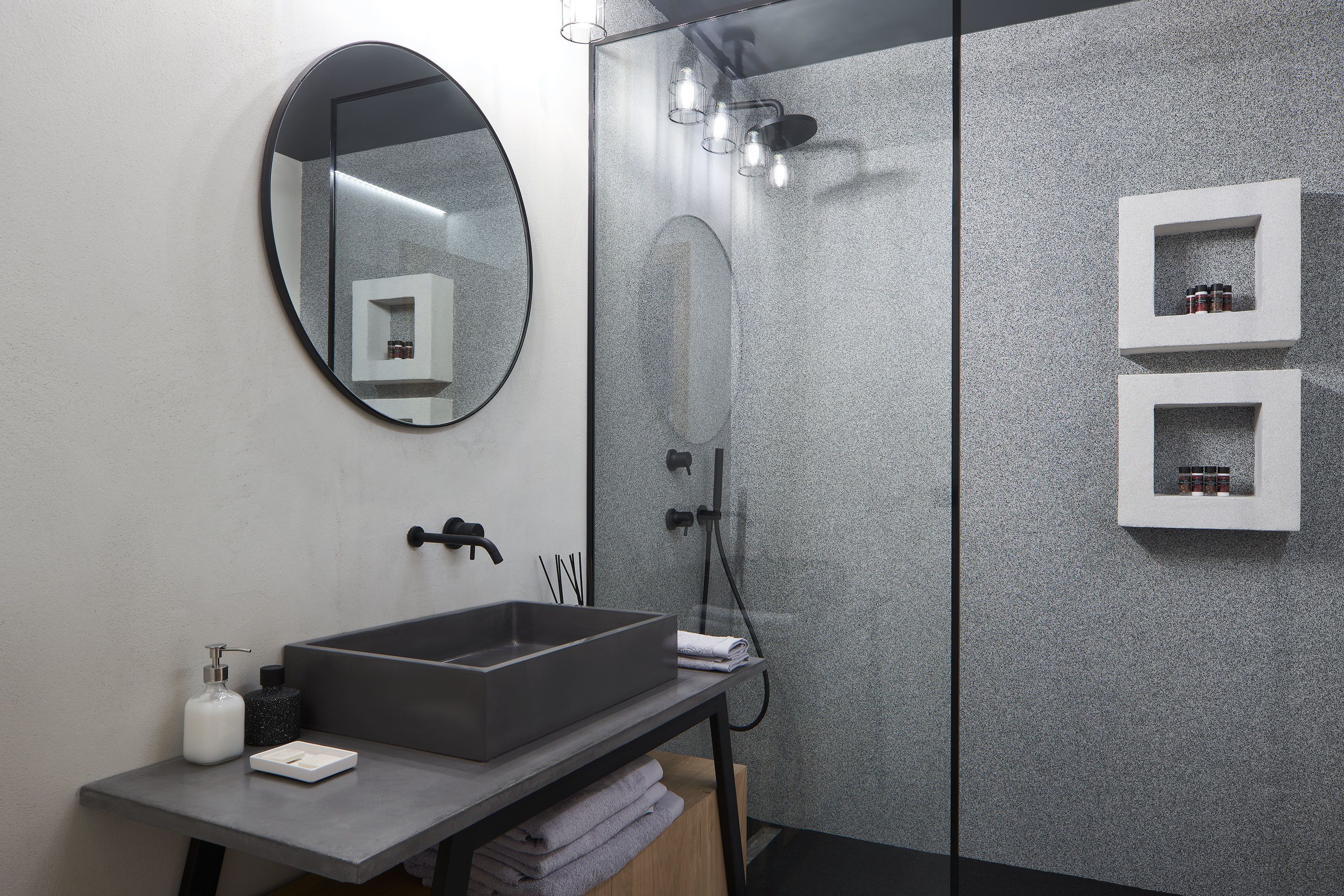 A modern bathroom with a rectangular sink, a round mirror, and a glass-enclosed shower.