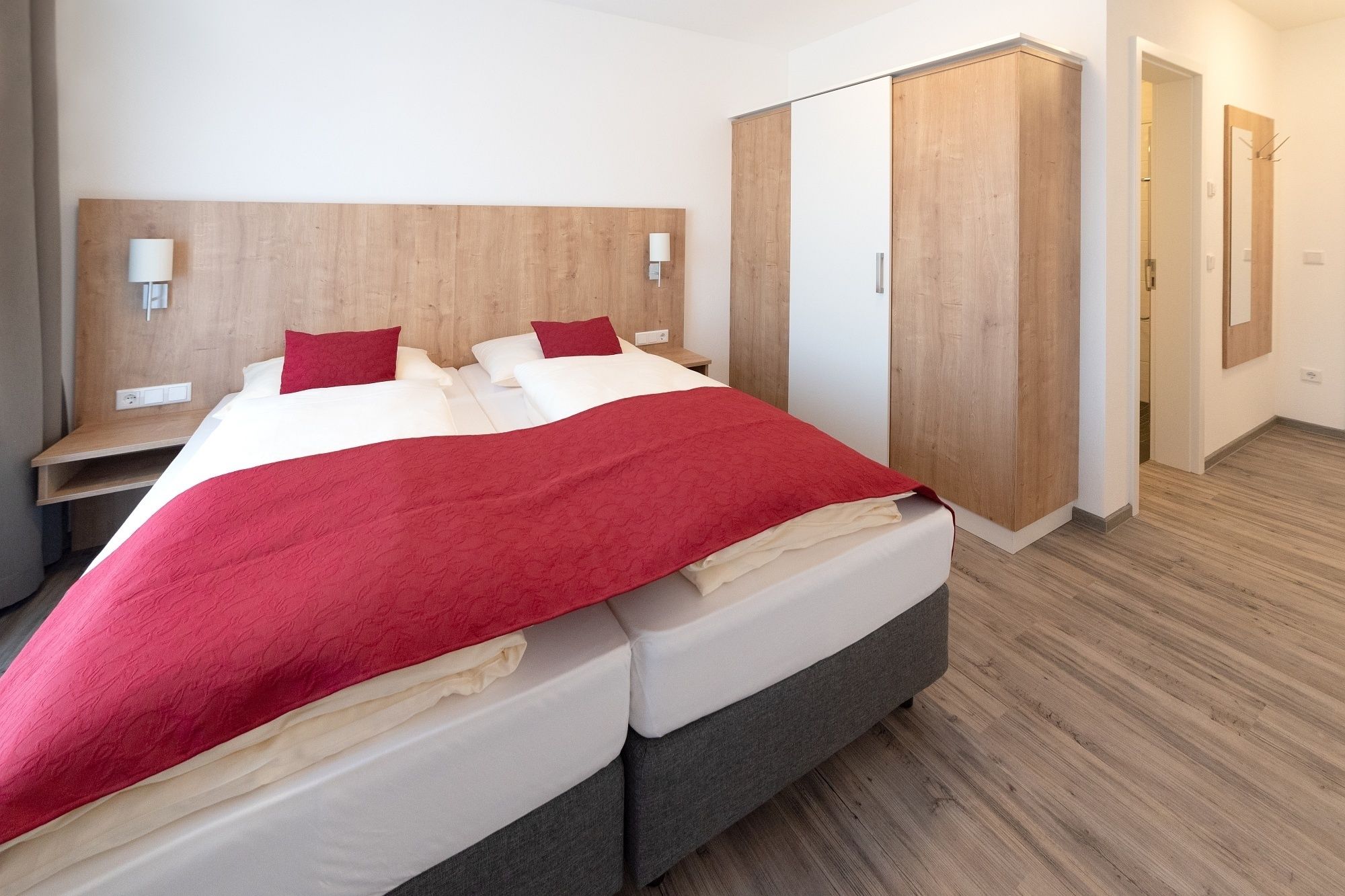 Una habitación de hotel moderna con una cama grande, cabecera de madera, mesitas de noche y un armario.