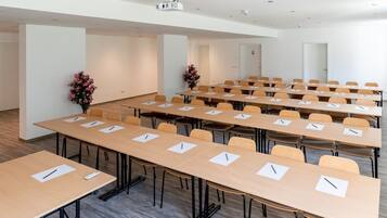 A conference room with multiple tables and chairs, equipped with pens and notepads, and a projector on the ceiling.