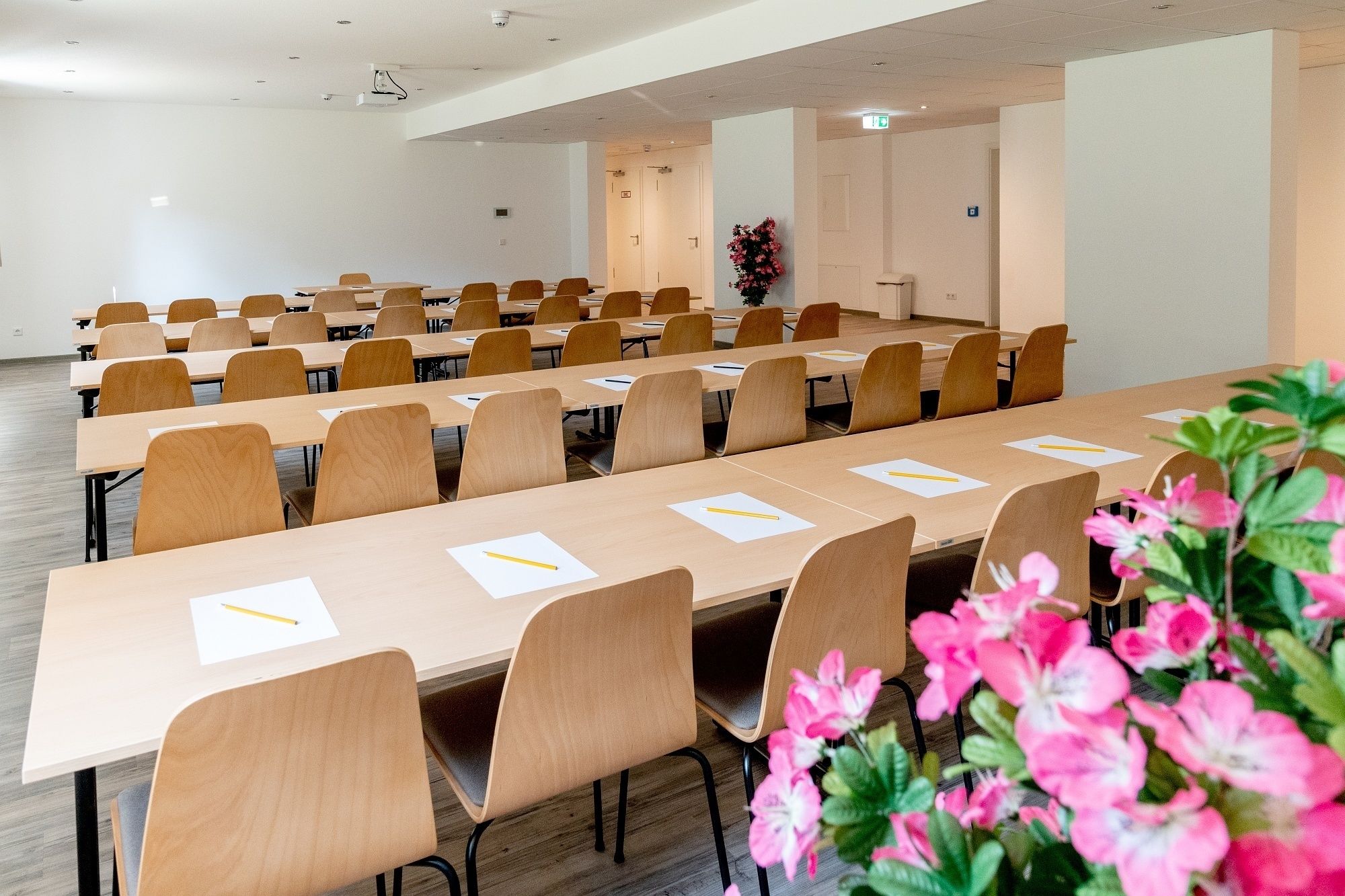 A conference room with long tables and chairs, equipped with projectors and a floral arrangement.