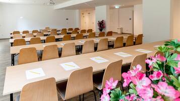A conference room with long tables and chairs, equipped with projectors and a floral arrangement.