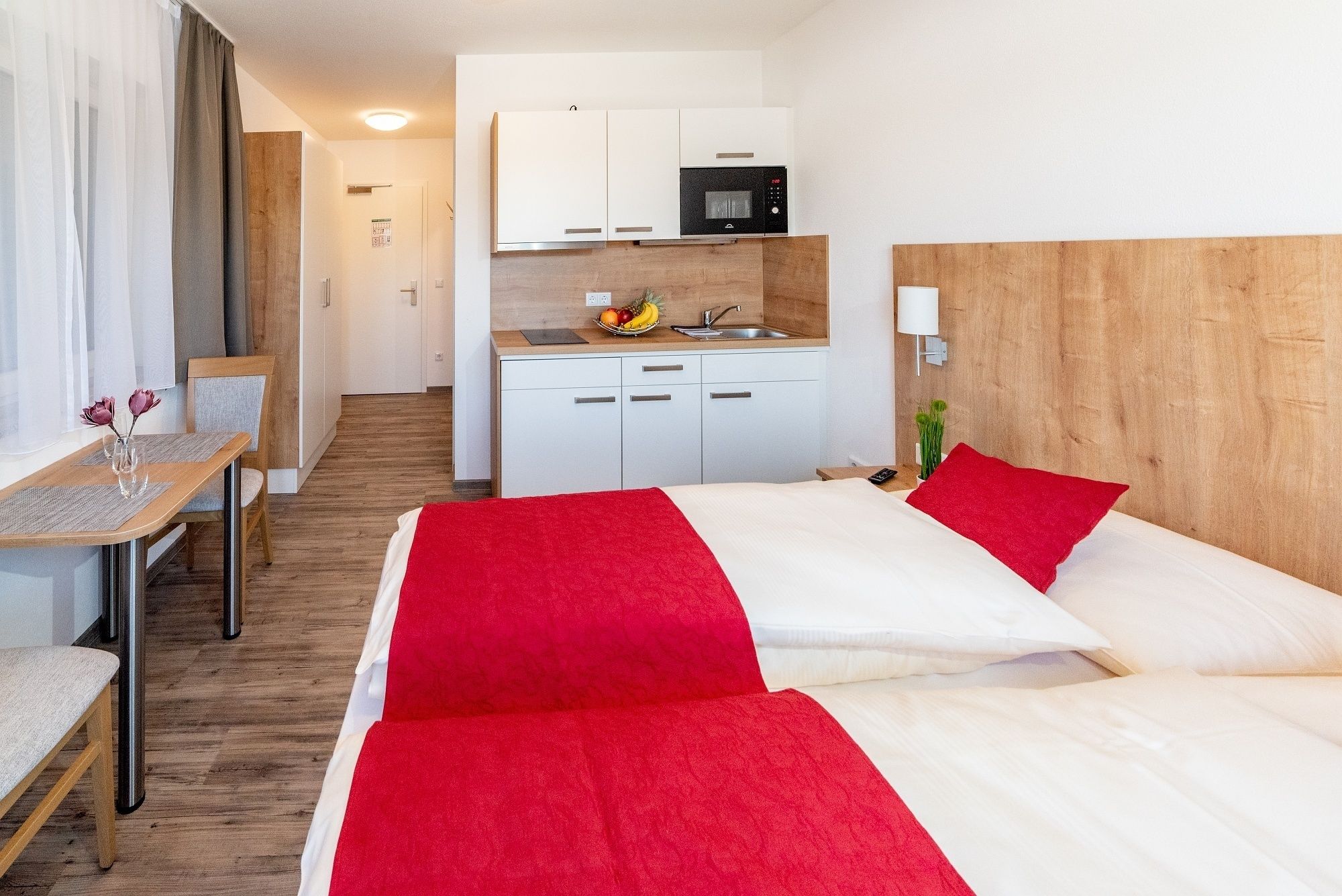 Una habitación de hotel con cama, escritorio, silla, kitchenette y baño.
