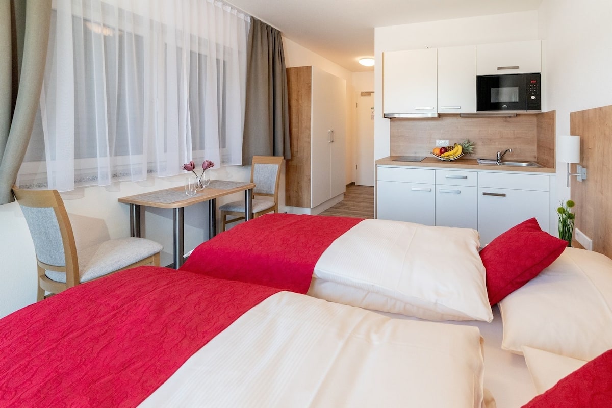 A hotel room with a bed, a small table with chairs, a kitchenette, and a bathroom.