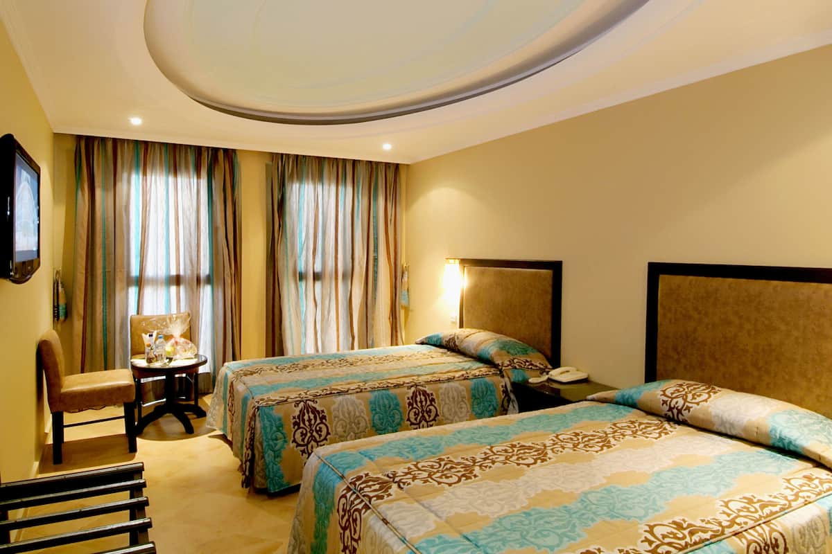 A hotel room with two beds, a desk, a chair, and a television.