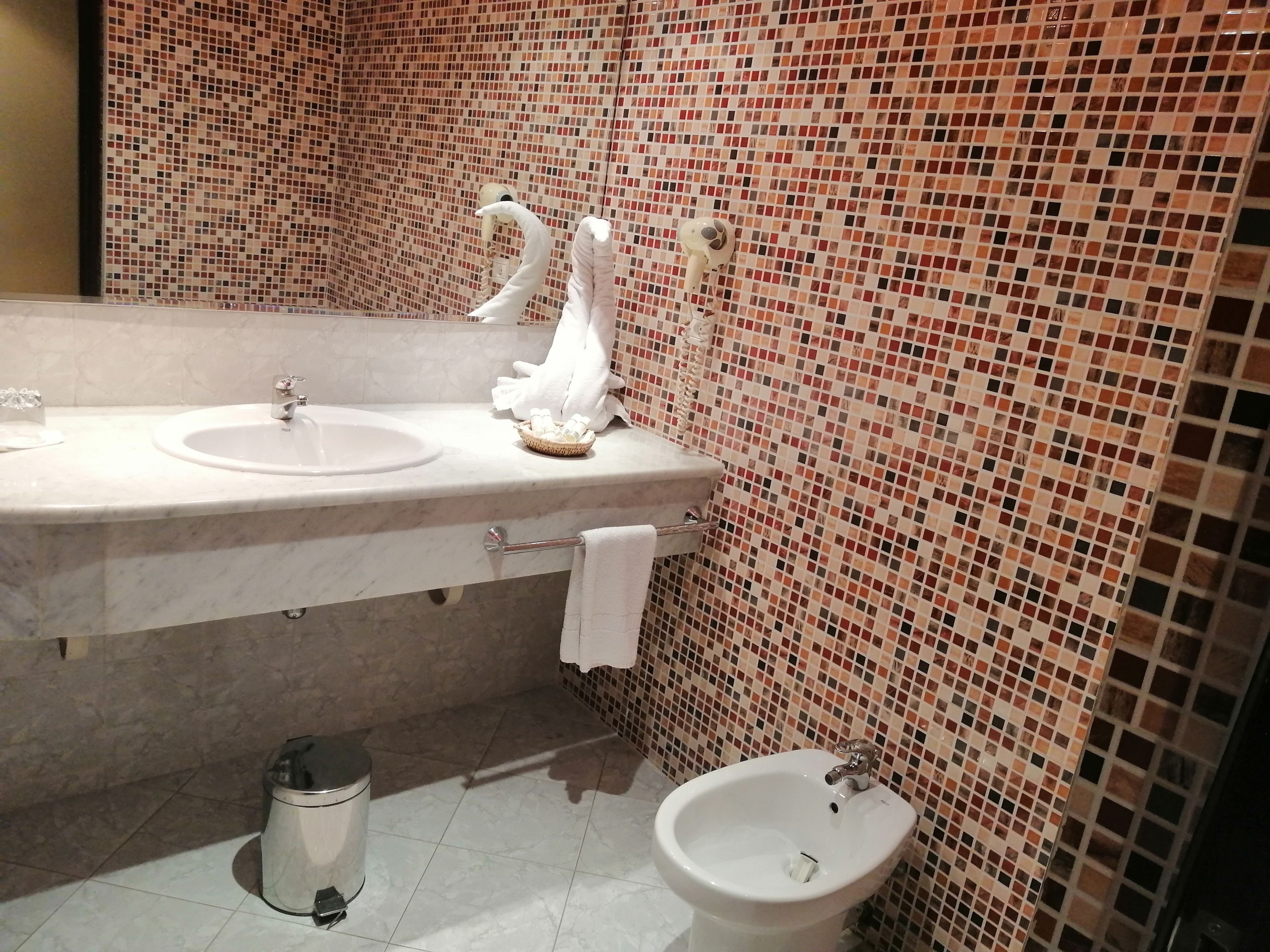 A bathroom with a marble sink, a bidet, and a mosaic-tiled wall.