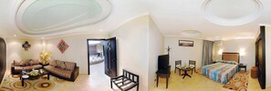 A living room with a sofa, coffee table, and decorative items. There is a dining area with a table and chairs. The room has a modern design with a large window and a door leading to another room. - Hotel Tghat (Fes)