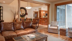 Ein Wohnzimmer mit einer Ledersofa, einem Couchtisch und einem Sessel. Es gibt einen Essbereich mit Tisch und Stühlen, und im Hintergrund eine Küche.