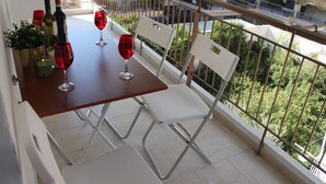 Ein Balkon mit einem Tisch für zwei Personen, zwei weiße Stühle, einem Blumentopf und zwei Weingläsern.