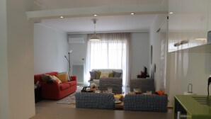 Ein modernes Wohnzimmer mit einem roten Sofa, grauen Sesseln, einem Couchtisch und einem Essbereich mit einem grünen Gerät.