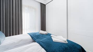 Habitación de hotel con una cama, una colcha azul acolchada, almohadas blancas y una toalla blanca doblada sobre la cama.