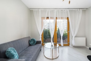 Un saló modern amb un sofà gris, una taula de centre de vidre i cortines blanques lleugeres.