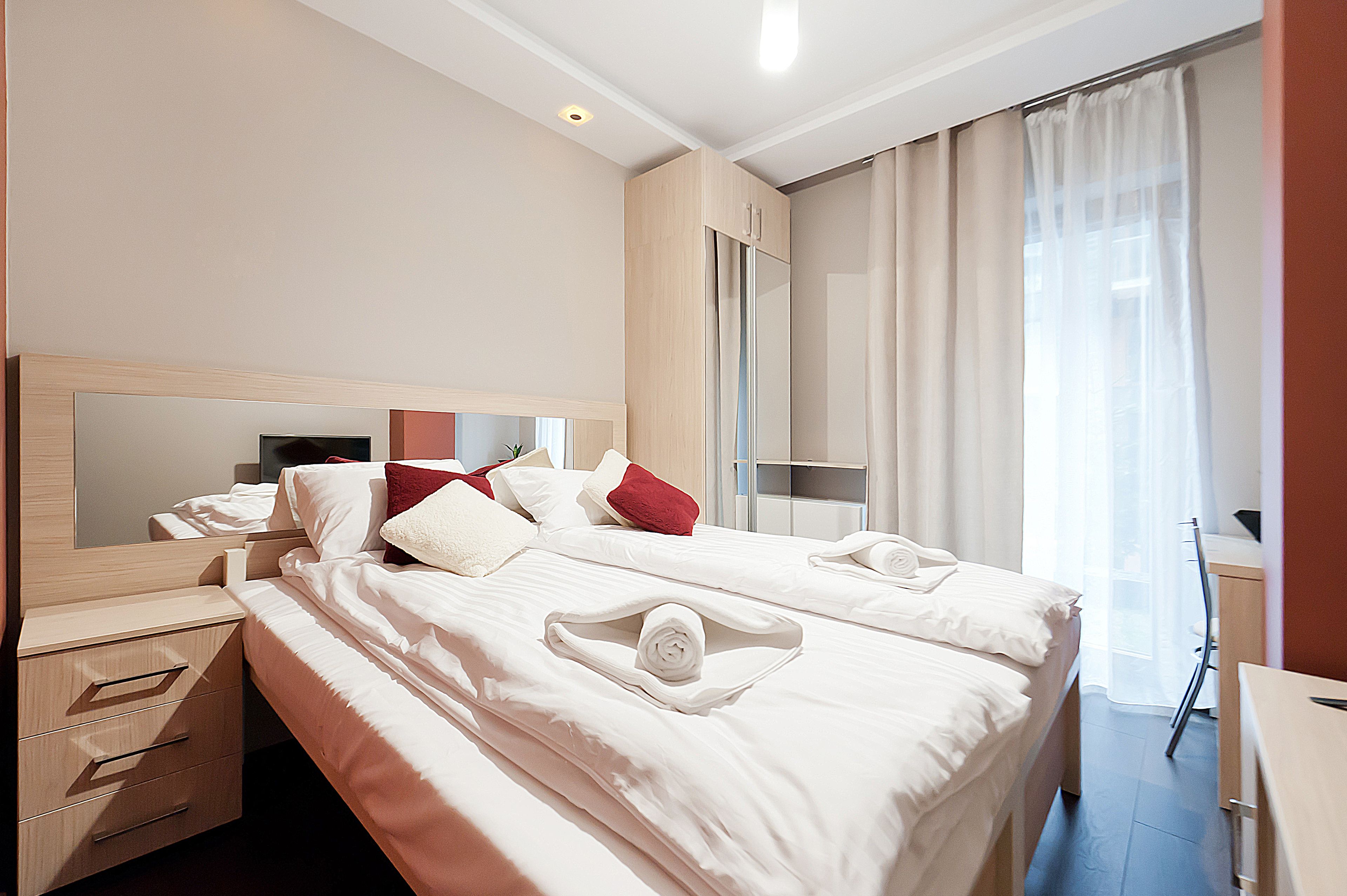 A hotel room with two beds, a desk, a chair, a mirror, and a window with curtains.