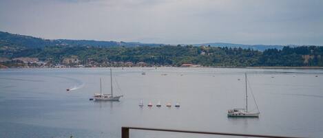 A coastal view with boats on the water, a distant shoreline with buildings, and a hilly landscape.