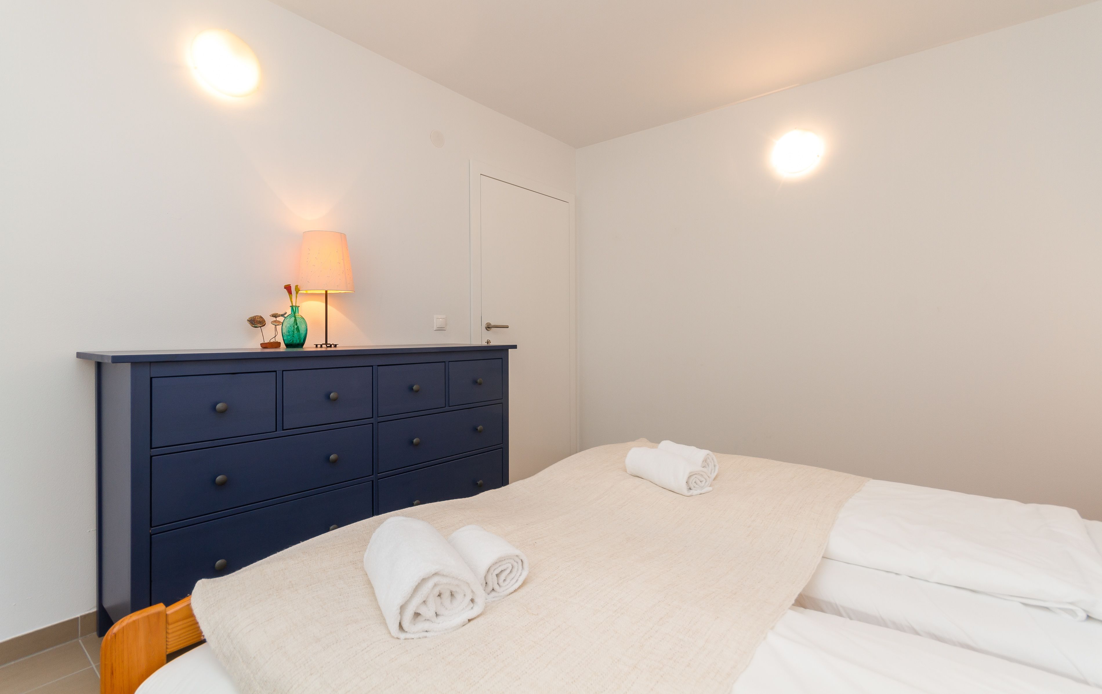 A bedroom with a bed, a dresser, a lamp, and two wall sconces.