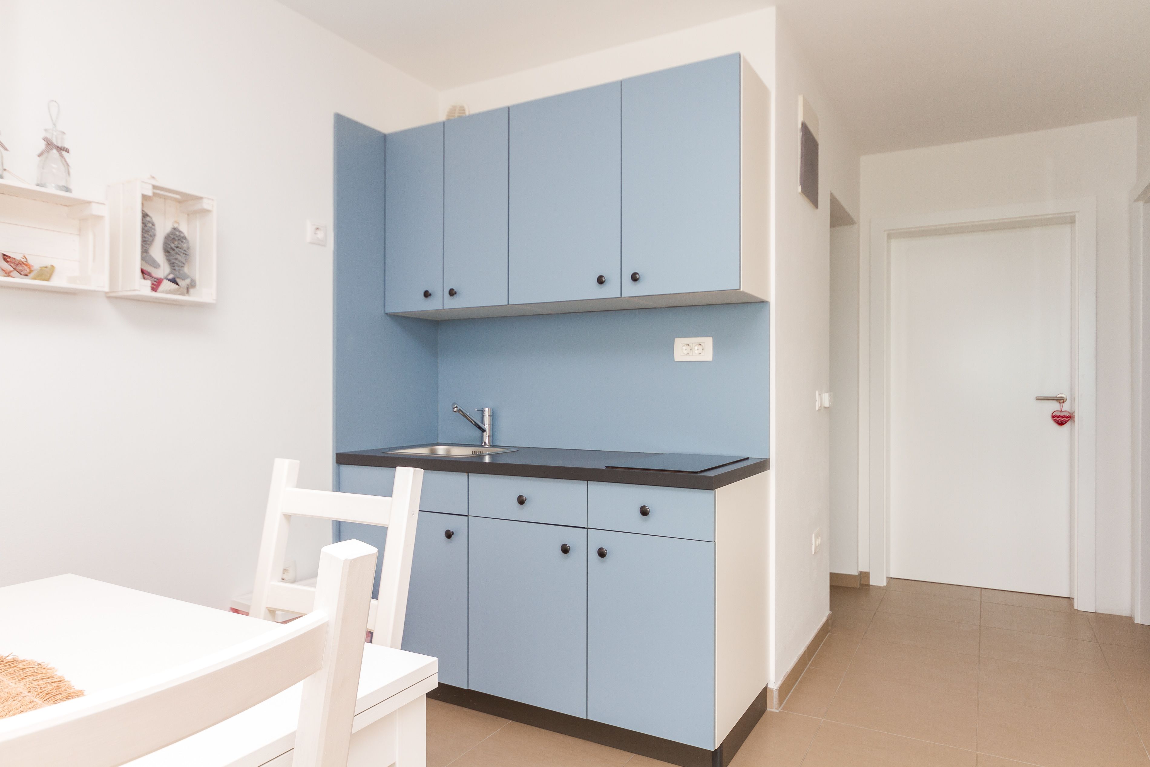 Een kleine keuken met blauwe kastjes, een wit aanrecht en een witte stoel.
