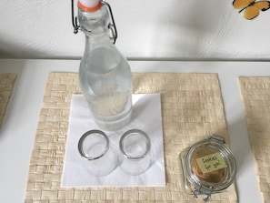A bottle of water, two empty glasses, and a jar with a note on a woven mat.