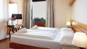 A hotel room with a bed, a desk with a lamp, and a view of the outside. - Parc Hotel Casa Mia (Lazise)