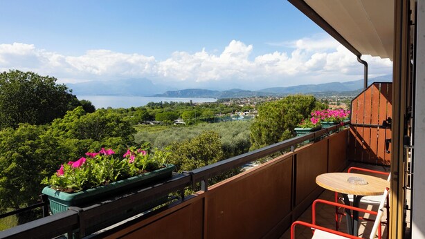 A balcony with a view of a lake, greenery, and distant mountains. - Parc Hotel Casa Mia (Lazise)