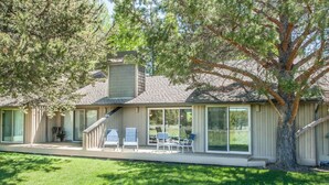 Ein eingeschossiges Haus mit überdachter Terrasse, großen Fenstern und einem Baum im Vordergrund.