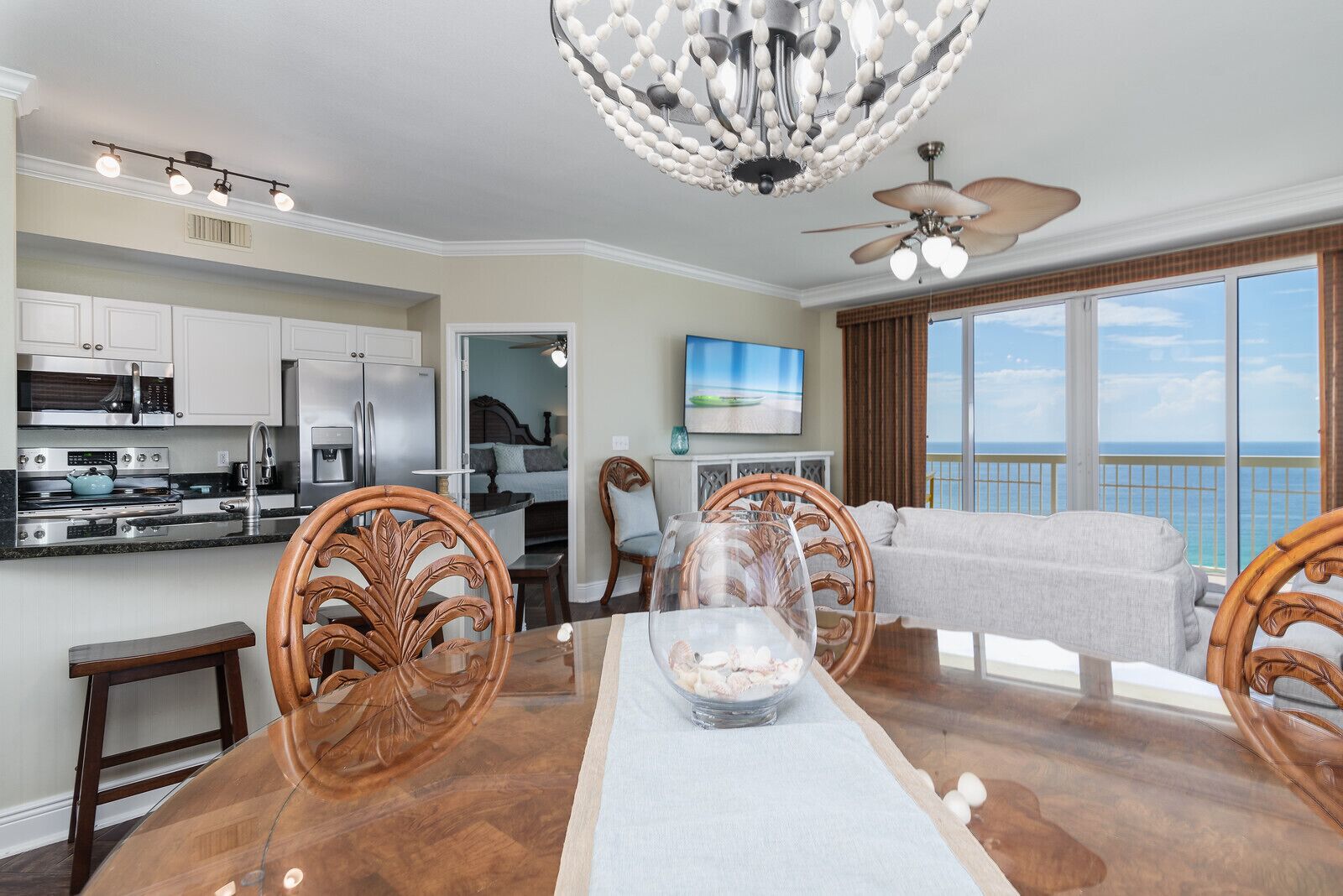A modern kitchen with stainless steel appliances, a dining area with a wooden table and chairs, and a balcony with a view of the ocean.