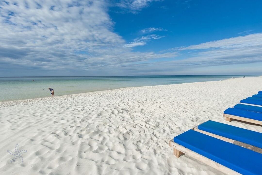 En strand med hvidt sand og en klar blå himmel. Der er blå liggestole langs stranden.