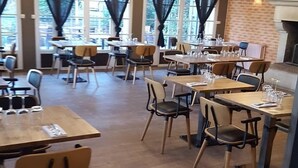 A restaurant with multiple tables and chairs, large windows with curtains, and brick walls. - Maison Arquier (Aix-en-Provence)