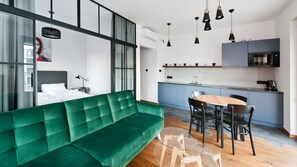 A modern living space with a green sofa, a dining table with chairs, a kitchen area, and a large window with curtains. - Apartamenty Sun & Snow Rakowicka Podkowa (Kraków)