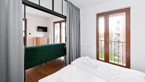 A bedroom with a bed, a green sofa, a wooden cabinet, a TV, and a window with a view of buildings. - Apartamenty Sun & Snow Rakowicka Podkowa (Kraków)