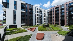 A modern apartment complex with multiple balconies, a landscaped courtyard with planters, and a central wooden bench. - Apartamenty Sun & Snow Rakowicka Podkowa (Kraków)