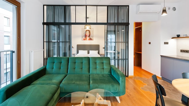 A modern living room with a green sectional sofa, a glass coffee table, and a dining area with a wooden table and chairs. - Apartamenty Sun & Snow Rakowicka Podkowa (Kraków)
