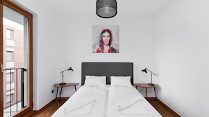A bedroom with a double bed, two bedside tables, a ceiling light fixture, and a window with a view of a brick building. - Apartamenty Sun & Snow Rakowicka Podkowa (Kraków)
