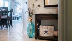 A hallway with a wooden console table displaying a 'BEACH' sign, a blue vase with dried plants, and a dining area in the background. - HS-1031 Experience ocean views, a spacious 2-BR condo in Myrtle Beach (Myrtle Beach)