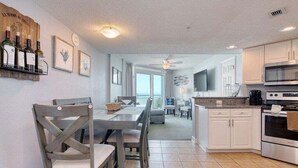 A modern kitchen with white cabinets, a dining area with a wooden table and chairs, and a view to a balcony. - HS-1031 Experience ocean views, a spacious 2-BR condo in Myrtle Beach (Myrtle Beach)