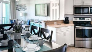 A modern kitchen with white cabinets, a stainless steel oven, and a microwave. There is a dining table with chairs and a small plant on the table. - HS-1031 Experience ocean views, a spacious 2-BR condo in Myrtle Beach (Myrtle Beach)