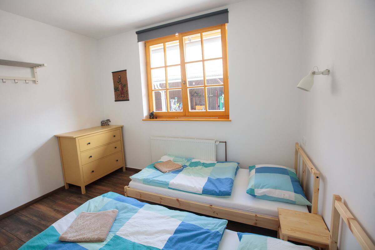 A bedroom with two beds, a dresser, a window with blinds, and a wall-mounted lamp.