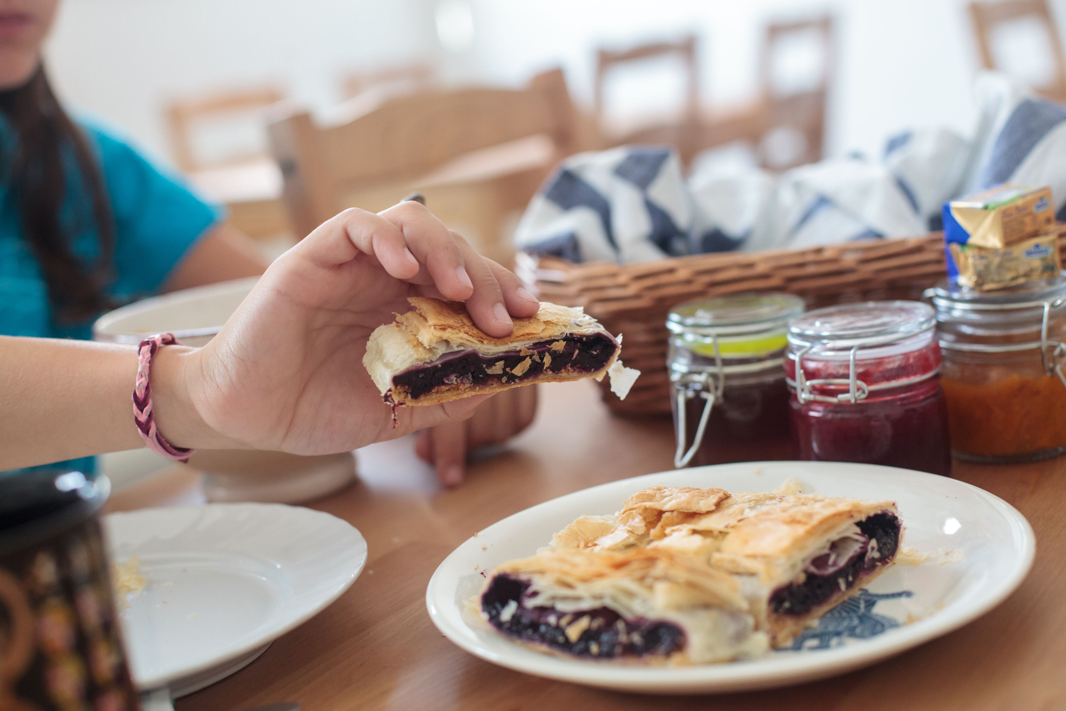 A dining table with a plate of food, a jar of jam, and a basket in the background.