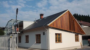 A white building with a sloped roof and wooden trim, featuring a glass balcony and a metal fence. - BikeSki B&B (Mežica)