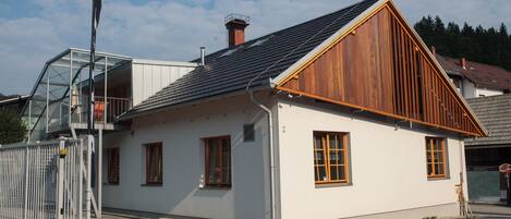 Ein weißes Gebäude mit geneigtem Dach und Holzelementen, das einen Glasbalkon und einen Metallzaun zeigt.