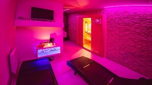 A spa room with a stone wall, a massage table, a small counter with a TV, and a door leading to a shower area. - BikeSki B&B (Mežica)