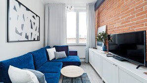 A modern living room with a blue sofa, a round coffee table, a flat-screen TV, and a brick wall.