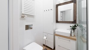 A modern bathroom with a white toilet, a sink with a wooden countertop, a mirror, and a radiator.