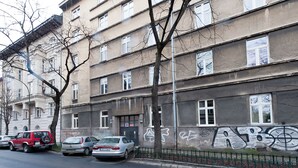 A multi-story building with graffiti on the lower wall, parked cars along the street, and a tree in front.