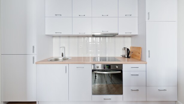 A modern kitchen with white cabinetry, a stainless steel sink, a built-in oven, and a wooden countertop.