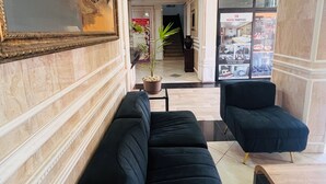 Een hotellobby met een zwarte bank, een potplant, een ingelijste afbeelding en een trap naar de verdiepingen erboven.