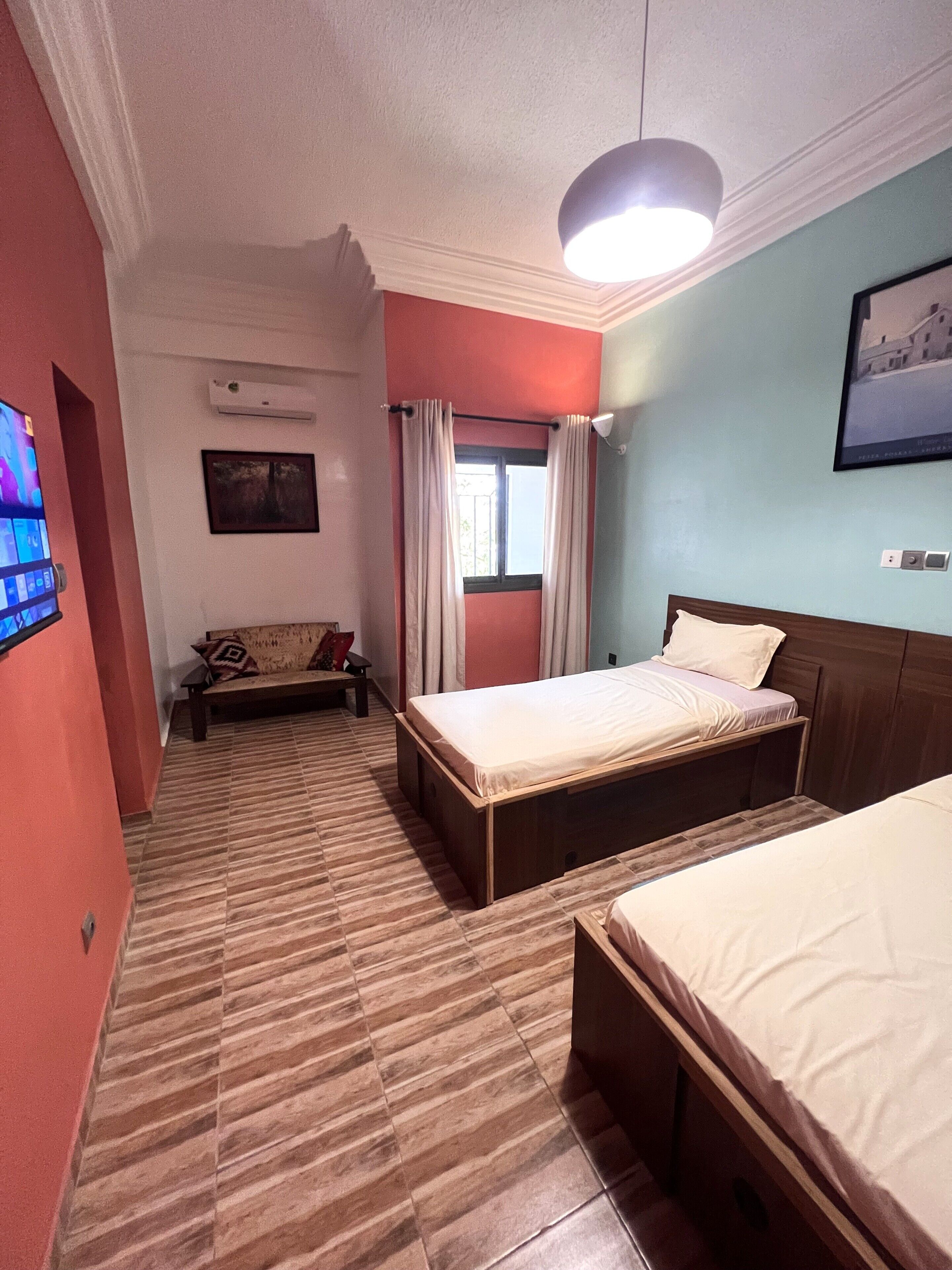 Habitación de hotel con dos camas, un televisor, una ventana con cortinas, un sofá y un equipo de aire acondicionado.