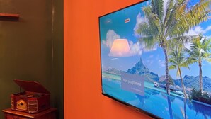 Een kamer met een televisie waarop een tropisch tafereel te zien is, een houten dressoir en een houten vloer.